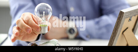 Male arm holding lightbulb over tip can full of US money Stock Photo