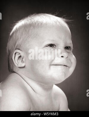 1960s SMILING HAPPY BABY 3/4 PROFILE PORTRAIT - b21518 HAR001 HARS B&W HAPPINESS HEAD AND SHOULDERS CHEERFUL ENGAGED SMILES ENGROSSED CONCEPTUAL JOYFUL BABY BOY GROWTH JUVENILES ATTENTIVE BLACK AND WHITE CAUCASIAN ETHNICITY HAR001 OLD FASHIONED Stock Photo