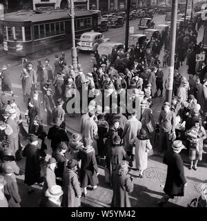 1930s BUSY CROWD MEN AND WOMEN PEDESTRIANS CROSSING CITY STREET INTERSECTION CARS AND TROLLY IN BACKGROUND PHILADELPHIA PA USA  - c1073 HAR001 HARS MALES CORNER PEDESTRIANS TRANSPORTATION B&W NORTH AMERICA NORTH AMERICAN WIDE ANGLE HIGH ANGLE ADVENTURE INTERSECTION AND PA DIRECTION CONGESTED IN TAXI CAB CONCEPTUAL ESCAPE VOTERS BLACK AND WHITE CITIZENS HAR001 OLD FASHIONED TROLLY Stock Photo