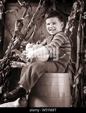 1940s SMILING HAPPY BOY SITTING ON BARREL HOLDING AUTUMN HARVEST PUMPKIN LOOKING AT CAMERA - c1722 HAR001 HARS BARREL EXPRESSIONS AGRICULTURE B&W EYE CONTACT HAPPINESS CHEERFUL EXCITEMENT ON SMILES CONCEPTUAL JOYFUL STYLISH GROWTH JUVENILES BLACK AND WHITE CAUCASIAN ETHNICITY HAR001 OLD FASHIONED Stock Photo