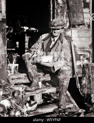 1920s 1930s MAN PROFESSIONAL MARKET HUNTER SITTING ON SHACK STEPS  PAINTING CANVAS BACK DUCK DECOYS BARNEGAT BAY NEW JERSEY USA - d2269 HAR001 HARS RURAL COPY SPACE FULL-LENGTH PERSONS MALES HUNTER PROFESSION ROUGH CONFIDENCE B&W SKILL OCCUPATION SKILLS RUSTIC STRENGTH CAREERS EXTERIOR KNOWLEDGE PRIDE ON AUTHORITY DECOY NJ OCCUPATIONS SHACK BAY MAN CONCEPTUAL DECOYS STYLISH NEW JERSEY CREATIVITY FIREARM FIREARMS MID-ADULT MID-ADULT MAN BARNEGAT BAY BLACK AND WHITE CAUCASIAN ETHNICITY HAR001 OLD FASHIONED Stock Photo