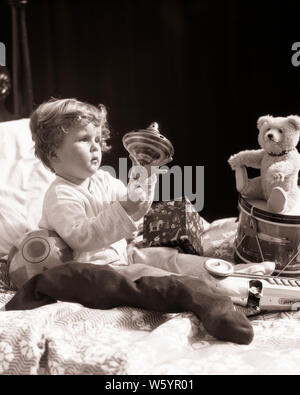 1920s 1930s TODDLER BOY IN BED PLAYING WITH MECHANICAL TOP SURROUNDED BY CHRISTMAS STOCKING TOY BEAR DRUM PRESSED TIN RACE CAR - j5026 HAR001 HARS COPY SPACE FULL-LENGTH MALES MECHANICAL B&W MORNING DREAMS HAPPINESS MERRY EXCITEMENT RECREATION SURROUNDED BY IN DECEMBER CONCEPTUAL DECEMBER 25 RACE CAR STYLISH BABY BOY JOYOUS JUVENILES BLACK AND WHITE CAUCASIAN ETHNICITY HAR001 OLD FASHIONED Stock Photo