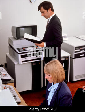 1980s OFFICE WITH EARLY COMPUTER HARDWARE WOMAN SEATED AT TERMINAL KEYBOARD MAN STANDING READING MANUAL - ko1320 PHT001 HARS KEYBOARD TECHNOLOGY TEAMWORK INFORMATION LIFESTYLE HISTORY FEMALES JOBS COMMUNICATING SEATED UNITED STATES COPY SPACE HALF-LENGTH LADIES COMPUTERS PERSONS MALES CONFIDENCE SCREENS BUSINESSWOMAN NORTH AMERICA WORK PLACE NORTH AMERICAN SKILL SUIT AND TIE OCCUPATION SELLING SKILLS HIGH ANGLE EARLY MANUAL NETWORKING MONITORS PROGRESS INNOVATION PRIDE OPPORTUNITY AUTHORITY OCCUPATIONS HIGH TECH CONNECTION ELECTRIC APPLIANCE HARDWARE STYLISH BUSINESSWOMEN TEXAS INSTRUMENTS Stock Photo