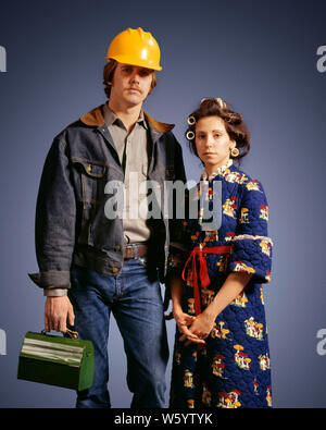 1970s UNSMILING AMERICAN GOTHIC MAN IN HARD HAT DENIM READY FOR WORK WOMAN ROLLERS IN HAIR WEARING HOUSECOAT LOOKING AT CAMERA - ks12292 HAR001 HARS NOSTALGIA OLD FASHION 1 SILLY STYLE COMIC SAFETY TEAMWORK COTTON LIFESTYLE FEMALES READY MARRIED STUDIO SHOT RURAL SPOUSE HUSBANDS HOME LIFE COPY SPACE FRIENDSHIP HALF-LENGTH LADIES PERSONS MALES AMERICANA DENIM MORNING PARTNER SADNESS ROLLERS EYE CONTACT BLUE COLLAR HOMEMAKER CURLERS HUMOROUS HOMEMAKERS MANUAL COMICAL LABOR EMPLOYMENT HOUSEWIVES OCCUPATIONS CONNECTION CONCEPTUAL COMEDY MIDDLE CLASS EMPLOYEE BLUE JEANS COOPERATION HOUSECOAT Stock Photo