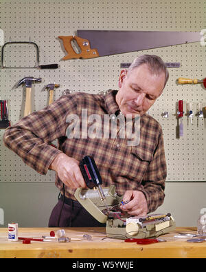 1960s SMILING HANDYMAN SENIOR MAN HOLDING USING A SOLDERING IRON TOOL IN HOME OR GARAGE SHOP REPAIRING PORTABLE RADIO - ks3178 HAR001 HARS COPY SPACE HALF-LENGTH PERSONS CARING MALES PROFESSION SENIOR MAN SENIOR ADULT PORTABLE SKILL OCCUPATION SKILLS OLDSTERS OLDSTER CAREERS RECREATION A IN OCCUPATIONS USING ELDERS REPAIRING DIY ELDERLY MAN OR PLAID SHIRT SAWS SOLDERING SOLUTIONS WORKSHOP CAUCASIAN ETHNICITY HANDYMAN HAR001 OLD FASHIONED Stock Photo
