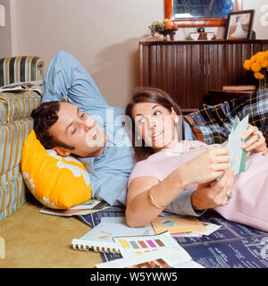 1970s COUPLE MAN WOMAN HUSBAND WIFE LYING ON FLOOR REVIEWING PAINT CHIP COLORS BROCHURES BLUEPRINTS FOR REMODEL OR NEW HOME - ks7702 HAR001 HARS RUG PLEASED JOY LIFESTYLE SATISFACTION FEMALES HOUSES MARRIED SPOUSE HUSBANDS HOME LIFE COPY SPACE FRIENDSHIP HALF-LENGTH LADIES PERSONS INSPIRATION RESIDENTIAL MALES PLANNING BUILDINGS BLUEPRINTS PARTNER BRUNETTE GOALS VISION DREAMS HAPPINESS CHEERFUL HIGH ANGLE ADVENTURE NEW HOUSE LIVING ROOM BROCHURES EXCITEMENT ON FACIAL HAIR HOMES SMILES NEW HOME CHIP CONNECTION REVIEWING DESIGNING IMAGINATION JOYFUL RESIDENCE STYLISH RENOVATION OPINIONS OR Stock Photo