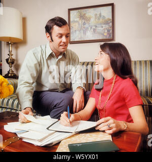 1970s SMILING COUPLE MAN WOMAN HUSBAND WIFE SITTING ON STRIPED COUCH REVIEWING FINANCES AND BILLS BALANCING CHECKBOOK CALENDAR  - ks7703 HAR001 HARS NOSTALGIA OLD FASHION FACIAL BUDGET COUCH STYLE COMMUNICATION TEAMWORK INFORMATION MYSTERY PLEASED JOY LIFESTYLE SATISFACTION FEMALES STRIPED MARRIED SPOUSE HUSBANDS HOME LIFE FINANCES COPY SPACE FRIENDSHIP HALF-LENGTH LADIES PERSONS MALES PLANNING CONFIDENCE PAYING EXPRESSIONS BALANCING PARTNER GOALS SUCCESS DREAMS HAPPINESS HEAD AND SHOULDERS CHEERFUL CHORE VICTORY STRATEGY AND LOW ANGLE PROGRESS CHECKBOOK ON FACIAL HAIR FEELING SMILES Stock Photo