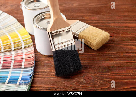 Two painting brushes, cans with paint, color guide palette on wooden table.