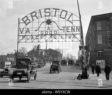 1900s 1920s SIGN ON ARCHWAY INDICATING STATE LINE BETWEEN BRISTOL VIRGINIA AND BRISTOL TENNESSEE DOWN MIDDLE OF MAIN STREET USA - q42680 CPC001 HARS CONNECTION CONCEPTUAL AUTOMOBILES CITIES VEHICLES BRISTOL ARCHWAY BOUNDARY COOPERATION TENNESSEE BLACK AND WHITE INDICATING MAIN STREET OLD FASHIONED Stock Photo