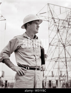1960s MAN SUPERVISOR WEARING WORK CLOTHES HARD HAT HOLDING CLIPBOARD UNDER HIS ARM POWER LINES AND TRANSFORMERS IN BACKGROUND - s14364 HAR001 HARS FACIAL CAREER POWER SAFETY ENGINEER LIFESTYLE JOBS RURAL MANAGER COPY SPACE HALF-LENGTH FROWN PERSONS MALES PROFESSION EXPRESSIONS B&W CONCERNED FROWNING ENERGY SKILL OCCUPATION SKILLS HIS STRENGTH CUSTOMER SERVICE HARD HAT AND CAREERS LEADERSHIP LOW ANGLE PROGRESS STERN PRIDE IN SUPERVISOR LINES OCCUPATIONS BOSSES INFRASTRUCTURE LINEMAN MID-ADULT MID-ADULT MAN TRANSFORMERS BLACK AND WHITE CAUCASIAN ETHNICITY GRID HAR001 OLD FASHIONED POWER LINES Stock Photo