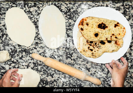 Chef preparing homemade Naan, indian or asian bread. Preparation process, dough on kitchen table and delicious breads ready to eat on white dish. Stock Photo