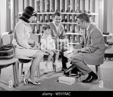 1960s 1970s FAMILY IN SHOE STORE SALESMAN SHOWING SHOE STYLE TO  UNHAPPY DAUGHTER AS SMILING FATHER AND MOTHER WATCH - s16875 HAR001 HARS SHOE INDOORS STRESS NOSTALGIC PAIR 4 SUBURBAN URBAN MOTHERS EXPRESSION OLD TIME BUSY NOSTALGIA OLD FASHION JUVENILE STYLE TEAMWORK FAMILIES LIFESTYLE FEMALES MARRIED SHOWING SPOUSE HUSBANDS FULL-LENGTH LADIES DAUGHTERS PERSONS CARING MALES FATHERS B&W PARTNER SHOPPER WIDE ANGLE SHOPPERS SELLING ADVENTURE CUSTOMER SERVICE AND CHOICE DADS AS IN TO AUTHORITY OCCUPATIONS KCAU CONCEPTUAL STYLISH FOOTWEAR COOPERATION GROWTH JUVENILES MID-ADULT MID-ADULT MAN Stock Photo