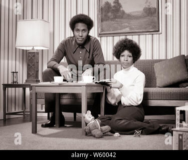 1970s AFRICAN-AMERICAN COUPLE AT COFFEE TABLE LOOKING AT CAMERA GOING OVER  FINANCES BILLS MAN ON SOFA WOMAN SITTING ON FLOOR - s19528 HAR001 HARS YOUNG ADULT BALANCE TEAMWORK FAMILIES LIFESTYLE SATISFACTION FEMALES MARRIED STUDIO SHOT SPOUSE HUSBANDS HOME LIFE FINANCES COPY SPACE FRIENDSHIP HALF-LENGTH LADIES MARRIAGE PERSONS INSPIRATION AFRO MALES DOLLHOUSE B&W PARTNER EYE CONTACT GOALS DREAMS AFRICAN-AMERICANS AFRICAN-AMERICAN HAIRSTYLE BLACK ETHNICITY PRIDE RELATIONSHIPS CONNECTION CONCEPTUAL FRO STYLISH COOPERATION SOLUTIONS TOGETHERNESS WIVES YOUNG ADULT MAN YOUNG ADULT WOMAN Stock Photo