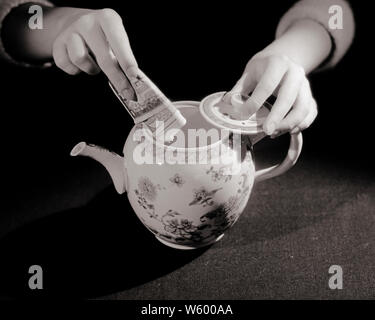 1930s WOMAN’S HANDS PUTTING CASH INTO TEAPOT HIDING MONEY OR TAKING MONEY OUT OF TEAPOT - s4396 HAR001 HARS WOMAN'S GOALS DREAMS HIGH ANGLE HIDE RAINY DAY CONCEPT CONCEPTUAL FUND HIDDEN CACHE OR SYMBOLIC TEAPOT CONCEPTS FUNDS TAKING OUT BLACK AND WHITE BORROWING CAUCASIAN ETHNICITY HANDS ONLY HAR001 OLD FASHIONED PAPER MONEY REPRESENTATION Stock Photo