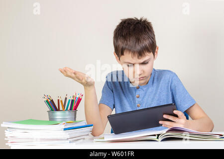 Confused,surprised child with tablet computer sitting at table with books notebooks Stock Photo