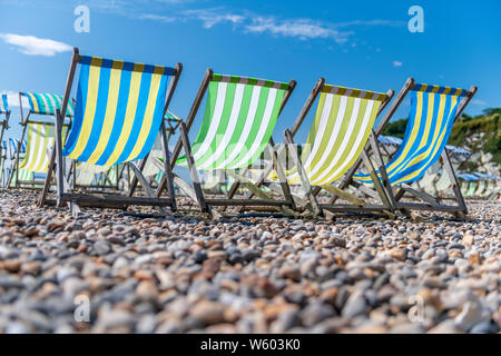 Four empty deckchairs sit on Beer beach in mid summer. Stock Photo