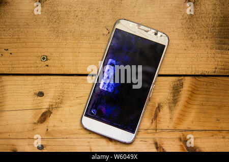 Top view of smartphone liquid-crystal display illuminated and broken on wood board background with copy space. Stock Photo