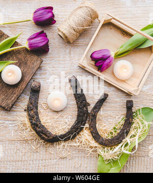 Flat lay view of two rusty small and big horseshoes on light wooden board background, decorated with white small candles. Horseshoe is good luck and p Stock Photo