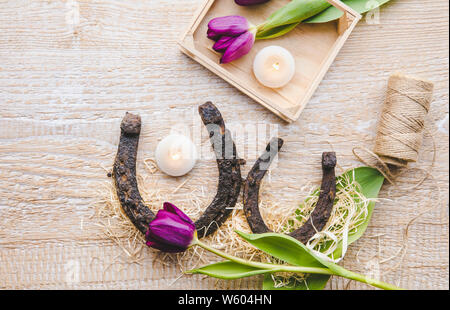 Flat lay view of two rusty small and big horseshoes on light wooden board background, decorated with white small candles. Horseshoe is good luck and p Stock Photo