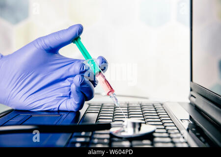 Selective focus on doctor hand wearing blue rubber glove and holding medical syringe needle in laptop computer keyboard. Online doctor or computer tec Stock Photo