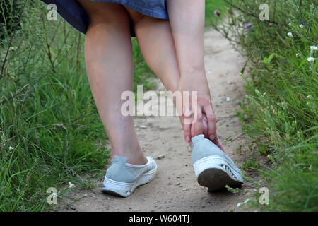 Heel pain, woman grabbed her foot while walking on a summer nature. Concept of pain in tired legs, injury or callus Stock Photo