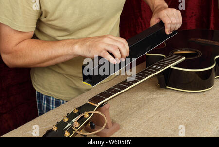 Musical instrument guitar repair and service - Worker grinds black guitar neck frets. Stock Photo