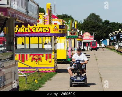 July 30, 2019, Des Moines, Iowa, U.S: A man rides by closed concession stands on the Iowa State Fair fairgrounds. The Iowa State Fair Is one of the largest state fairs in the United States and runs for 10 days. In 2019, it runs from August 8 to 18. More than one million people attend the fair every year. Most of the food concessions at the fair donâ€™t open until August 3, when exhibitors arrive, but the Westmoreland Concessions corn dog stand opened on July 28. One of the standâ€™s workers said a lot of people drive out to the fairgrounds the week before the fair to buy corn dogs because the Stock Photo