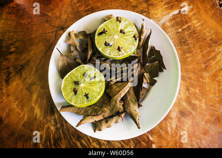 Natural repellent white plate with fresh lime, cloves and dried laurel on wooden table Stock Photo