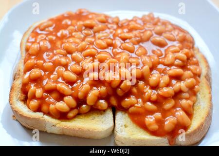 Baked beans in tomato sauce on thick white toast served on a white plate