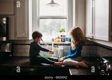 Young boy and girl sitting on counter in kitchen mixing muffin batter Stock Photo