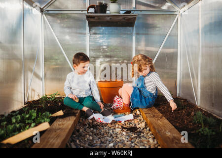 Young boy and girl sitting inside back yard green house in spring Stock Photo