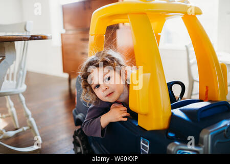 Young girl looking at camera sitting in toy car inside dining room Stock Photo