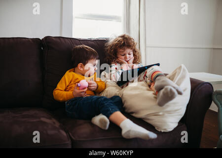 Young girl and boy sitting on couch together watching tablet Stock Photo