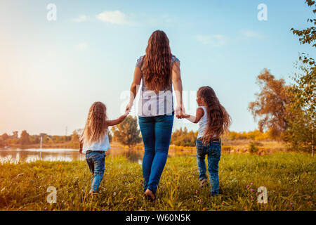 Family walking by summer river at sunset. Mother and her daughters having fun outdoors. Summer holidays Stock Photo