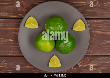 Group of three whole three pieces of fresh green lime on a ceramic grey plate flatlay on brown wood Stock Photo