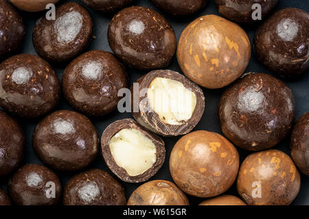 macadamia nuts in shell and dipped in dark chocolate on a black plate Stock Photo