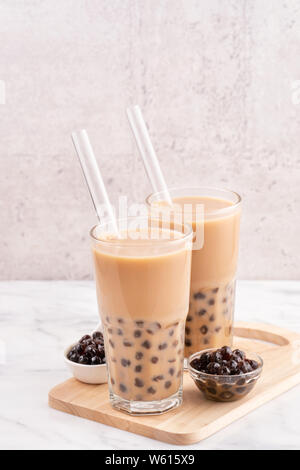 Tapioca pearl ball bubble milk tea, popular Taiwan drink, in drinking glass with straw on marble white table and wooden tray, close up, copy space. Stock Photo