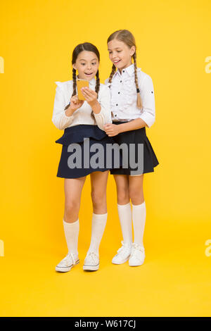 Girls school uniform using smartphone. Schoolgirls use mobile phone or smartphone to share photos. School application smartphone. Internet is wonderful resource but access to it has hazards for kids. Stock Photo