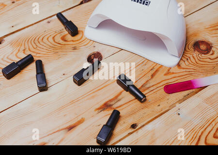 Nail Curing Lamp and different bottles of nail gel on wooden background. Shellac colours Stock Photo