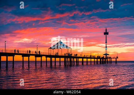 People walking along Brighton jetty with dramatic sunset on background after a hot summer day viwed from beach side, South Australia Stock Photo