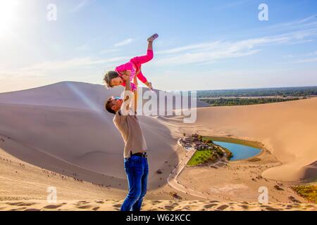 Tourists pose for photos near the Crescent Moon Lake, also known as Yueyaquan, surrounded by the Singing-Sand Dunes in the Gobi desert in Dunhuang, no Stock Photo