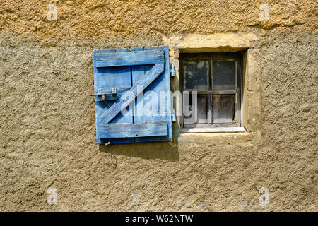 Old house window with open blue shutter in textured plaster wall.  Shutter features a Z shape structure Stock Photo
