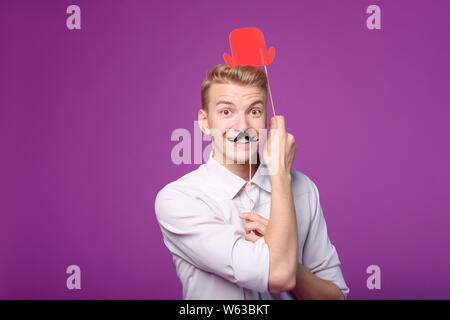 funny young man with paper mustache and red hat on background Stock Photo