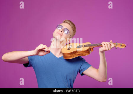 man with ukulele in hands on purple background plays like violin Stock Photo