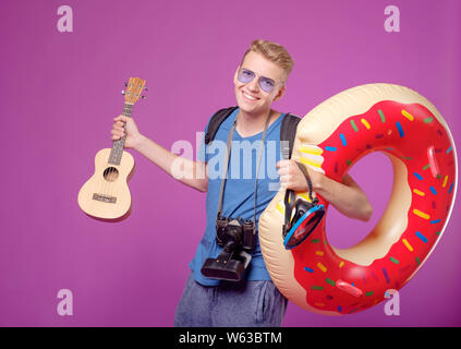 man traveler with camera, swimming circle and guitar ukulele on purple background Stock Photo