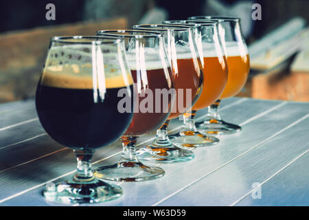 Glasses of different kinds of dark and light beer on wooden table in line. Cold delicious drinks are prepared for a big friend's party. Concept of drinks, fun, meeting, oktoberfest. Stock Photo