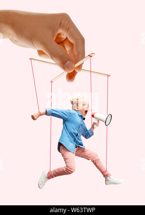 Girl like a puppet in somebodies hands on pink background. Concept of unfair manipulation, phycology of exploitation, mental technique, motivation. Puppets and their masters. Possessive relationship. Stock Photo