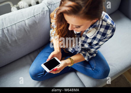 High angle shot of a beautiful woman sitting on sofa and looking at her phone, showing screen Stock Photo