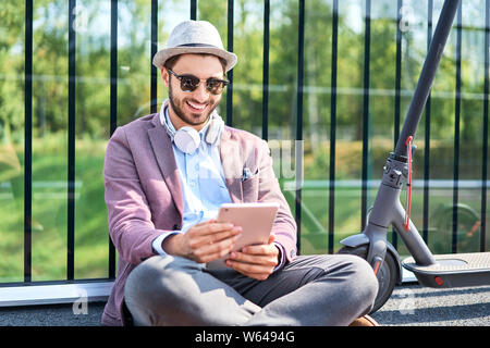 Picture of smiling man using digital tablet while sitting outdoors on sunny day Stock Photo