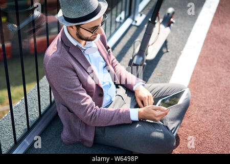 Stylish man sitting outdoors on sunny day and using tablet Stock Photo